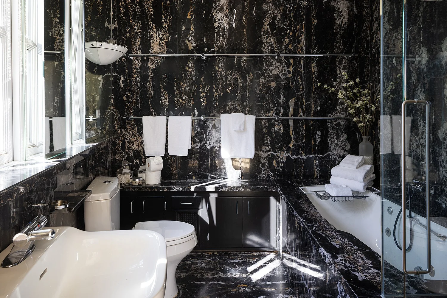 Black marble bathroom with tub, glass shower, and white towels