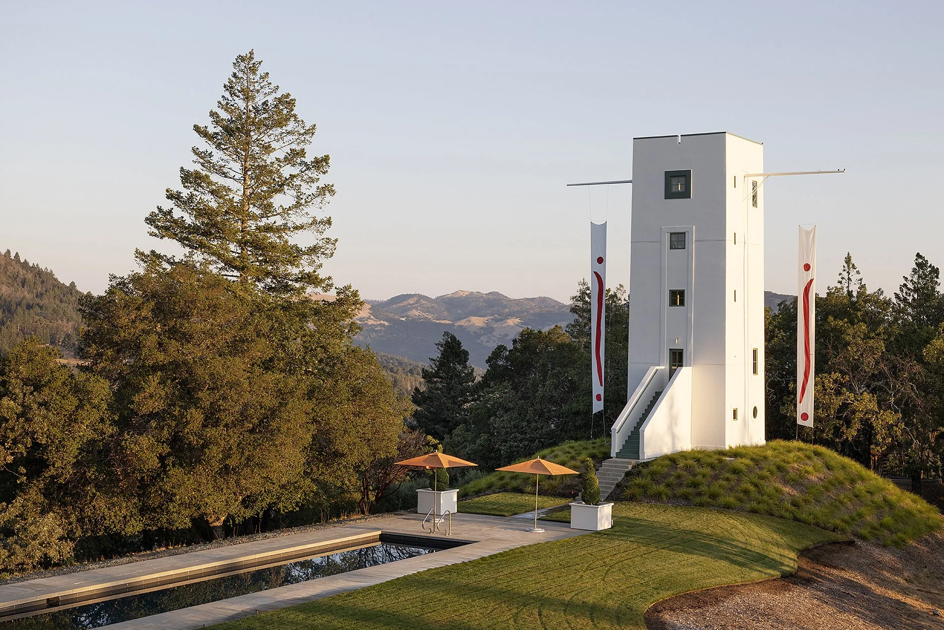 White tower beside a pool terrace and forested ridgeline